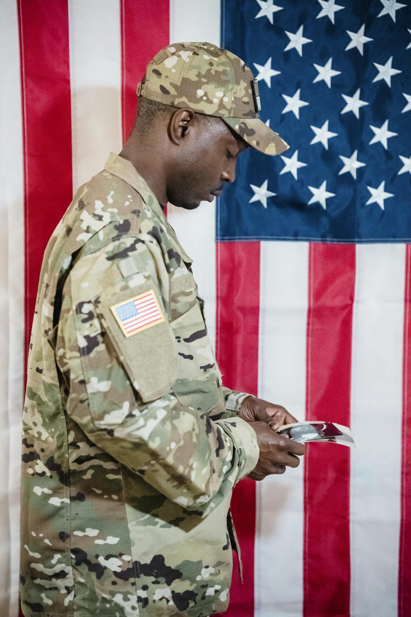 American soldier in camouflage uniform reading a document in front of the US flag.