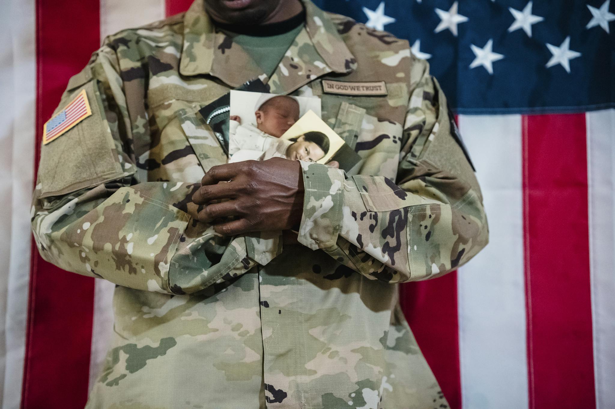 American soldier in uniform holding family photos against a flag backdrop.